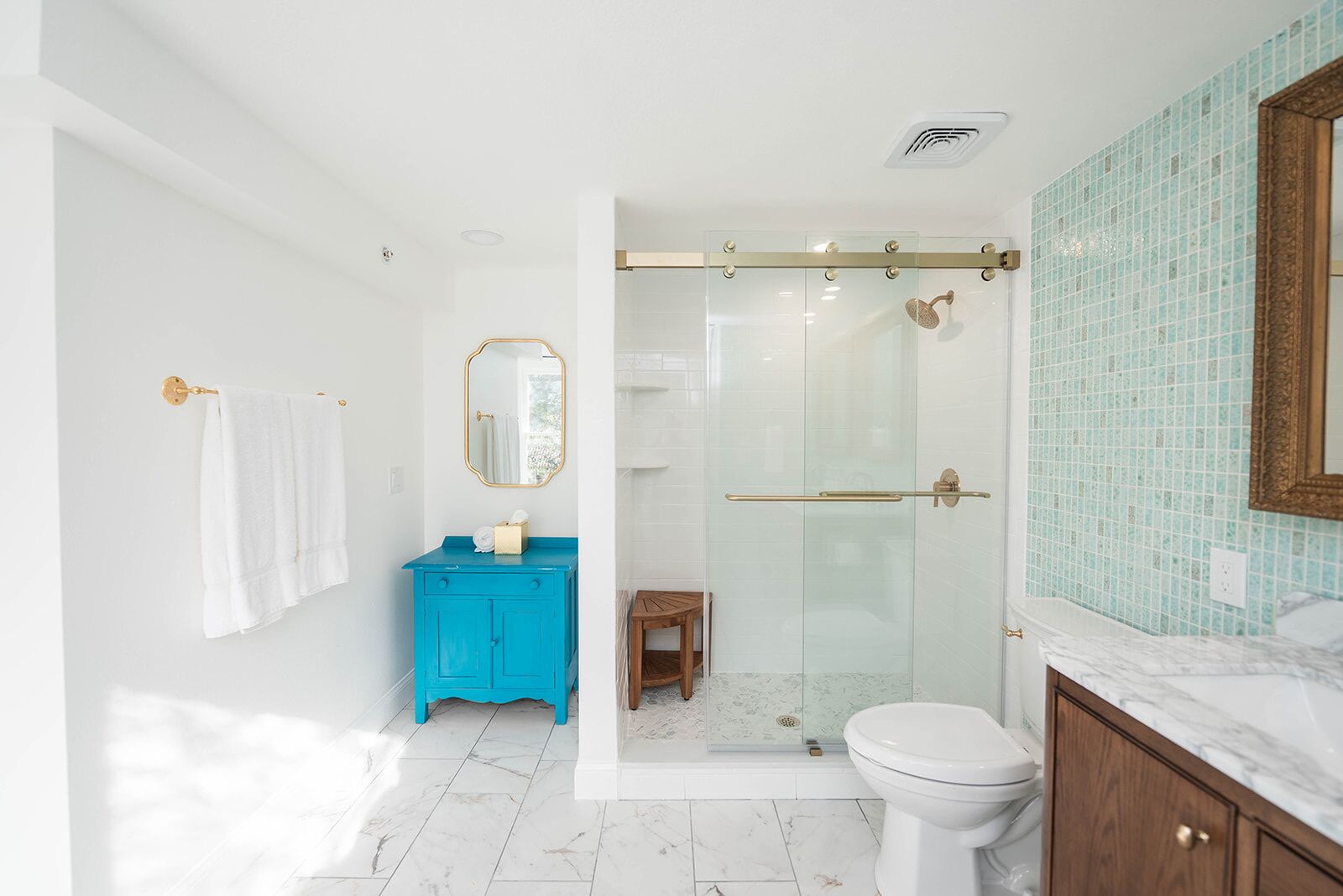 Une salle de bain moderne avec une douche à l’italienne en verre, des toilettes blanches, un meuble-lavabo bleu et un plan de toilette en marbre.