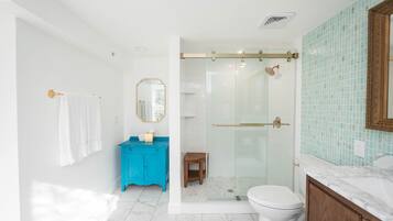 Une salle de bain moderne avec une douche à l’italienne en verre, des toilettes blanches, un meuble-lavabo bleu et un plan de toilette en marbre.
