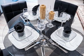 Une table ronde en verre, surmontée d’un chemin de table à carreaux noirs et blancs, entourée de chaises à revêtement noir et agrémentée de verres transparents.