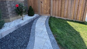 A pathway leading to a wooden gate, surrounded by a brick wall, a small tree, and a well-maintained lawn. - Luxury 2BR/2BA Modern B Apartment in Ajax, Toronto (Ajax)