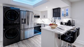 A modern kitchen with a skylight, stainless steel appliances, a central island, and black bar stools. - Luxury 2BR/2BA Modern B Apartment in Ajax, Toronto (Ajax)