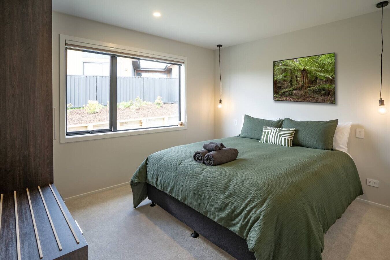 A bedroom with a large bed, a bench, a window with a view of a garden, and a painting on the wall.