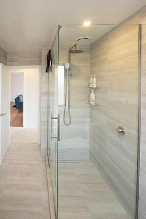 Une douche moderne dotée d’une porte en verre, d’un pommeau de douche à main et d’un panneau de commande fixé au mur.
