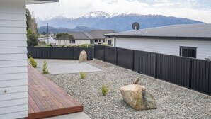 A residential area with a paved patio, a wooden deck, and a black fence. - NEW two bedroom home in Te Anau (Te Anau)