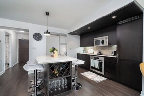 A modern kitchen with dark cabinetry, a white countertop, a built-in wine cooler, and a bar area with stools. - 2 BR + 2BA + Free Parking + Sofabed + Lakeview (Toronto)
