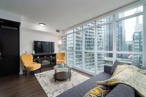 A modern living room with a large window, a sofa, two armchairs, a coffee table, and a flat-screen TV. - 2 BR + 2BA + Free Parking + Sofabed + Lakeview (Toronto)