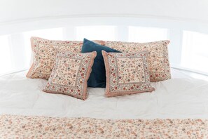 Ein Bett mit einem blumigen Überwurf und vier Kissen, eines davon ist einfarbig blau.