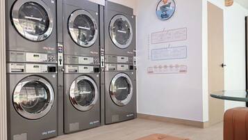 A laundry area with four 13kg washers and dryers, a small table, and a wall-mounted sign with instructions.