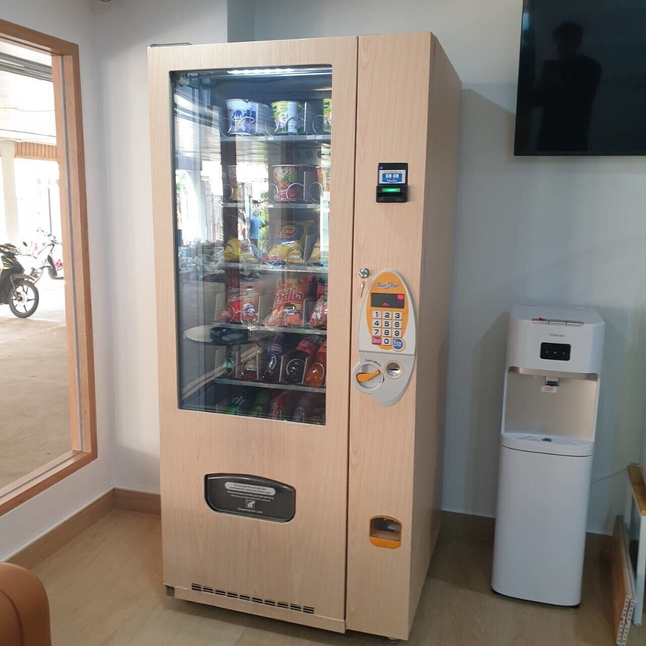 A vending machine with a glass front, a keypad, and a trash bin beside it.