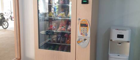 A vending machine with a glass front, a keypad, and a trash bin beside it.