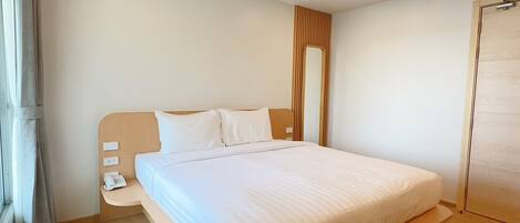 A modern hotel room with a large bed, a bedside table with a phone, and a window with curtains.