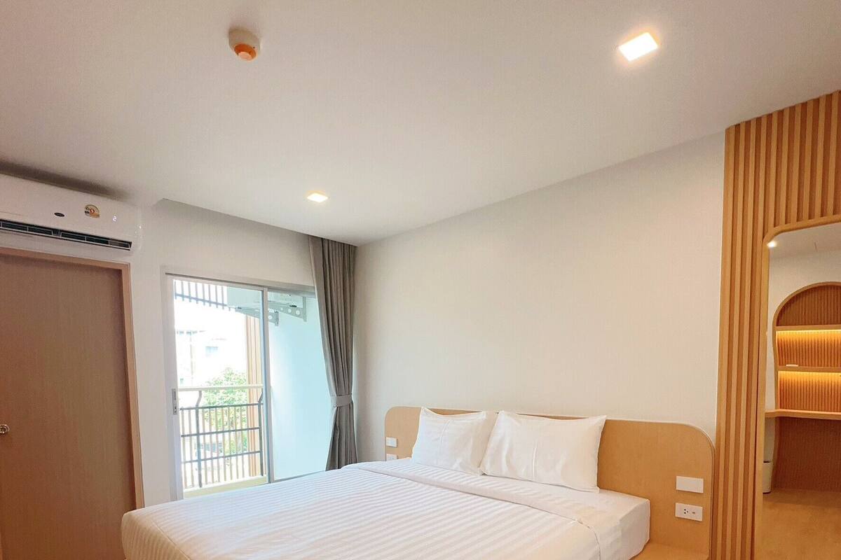 Quarto de hotel moderno com cama grande, piso de madeira, guarda-roupa embutido e espelho amplo.