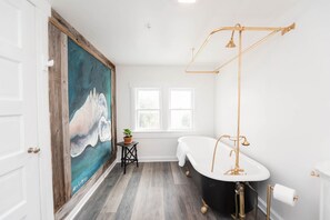 A bathroom with a freestanding bathtub, a large abstract painting, and a small table with a plant. - The Palmetto Room with Private Ensuite in Boutique B&B, The Parrish Grove Inn (Cocoa)