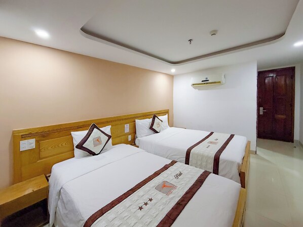 A hotel room with two beds, wooden headboards, white bedding, and a ceiling light fixture. - Quoc Thien Hotel Da Nang (Da Nang)