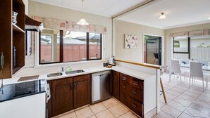 A modern kitchen with a dishwasher, a sink, and a dining area with a table and chairs. - Charming on Cambridge (Napier)