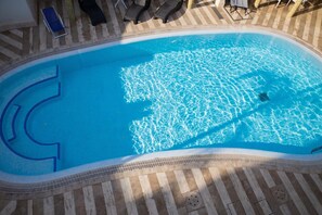 Una piscina con solárium empedrado y sillones de descanso.