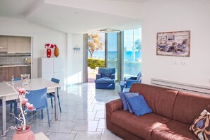 A modern living room with a brown sofa, a dining area with a white table, and a kitchen with white cabinets.