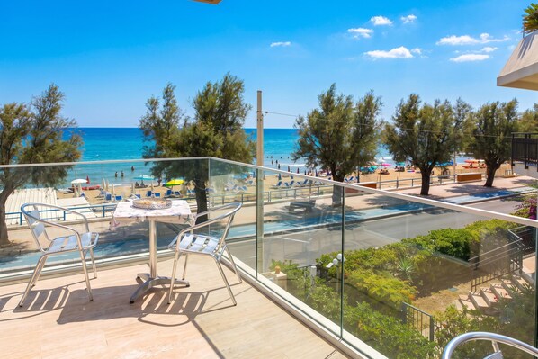 A balcony with a glass railing overlooking a beach with sun loungers and umbrellas.