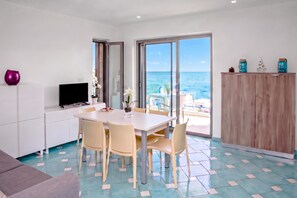 A modern kitchen with a dining area, a TV, and a view of the sea.