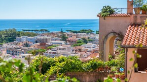 A coastal town with terracotta-roofed buildings, a prominent archway, and a view of the sea.