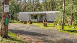 Una casa móvil con porche y una pequeña terraza, rodeada de árboles.