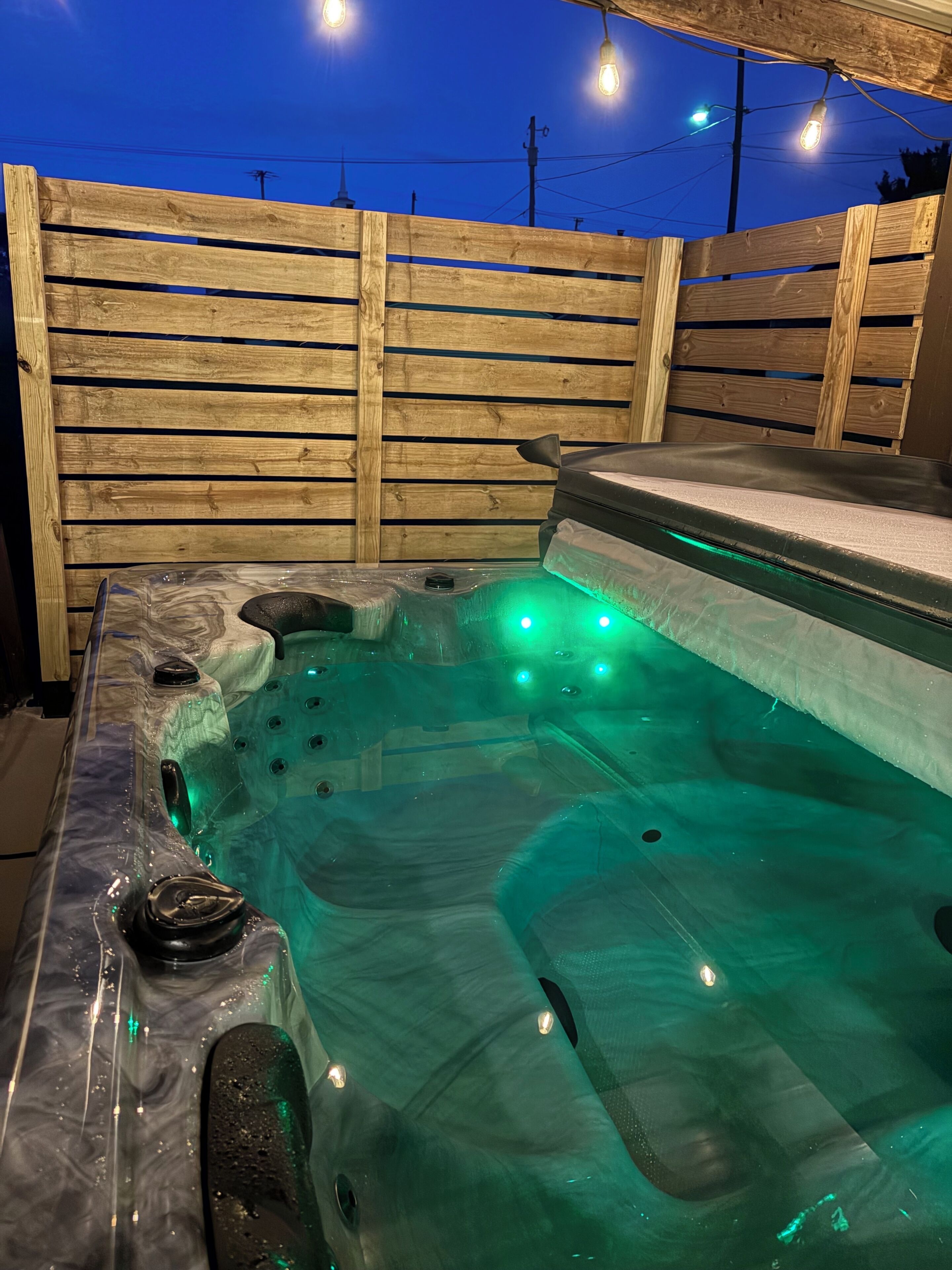 Ein Whirlpool mit grüner Beleuchtung, umgeben von einem Holzzaun.