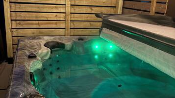Ein Whirlpool mit grüner Beleuchtung, umgeben von einem Holzzaun.