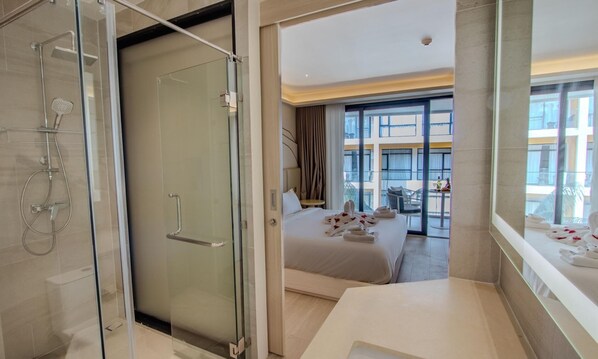 A modern hotel room with a glass shower enclosure, a bed with towels, and a view of the city through large windows.