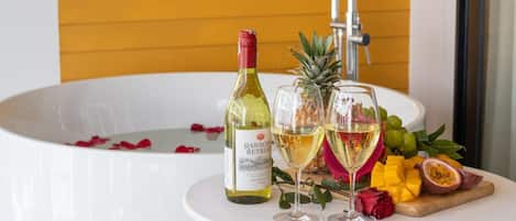Una bañera con una botella de vino y dos copas, rodeada de frutas y flores tropicales.