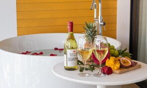 A bathtub with a bottle of wine and two glasses of wine, surrounded by tropical fruits and flowers.