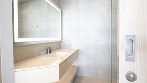 Un baño moderno con encimera color beige, un espejo grande y mampara de cristal.
