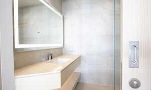 Une salle de bain moderne avec un comptoir de couleur beige, un grand miroir et une cabine de douche en verre.