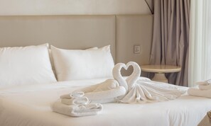 Une chambre d’hôtel avec un lit parfaitement fait, une petite table ronde et une serviette pliée en forme de cygne.