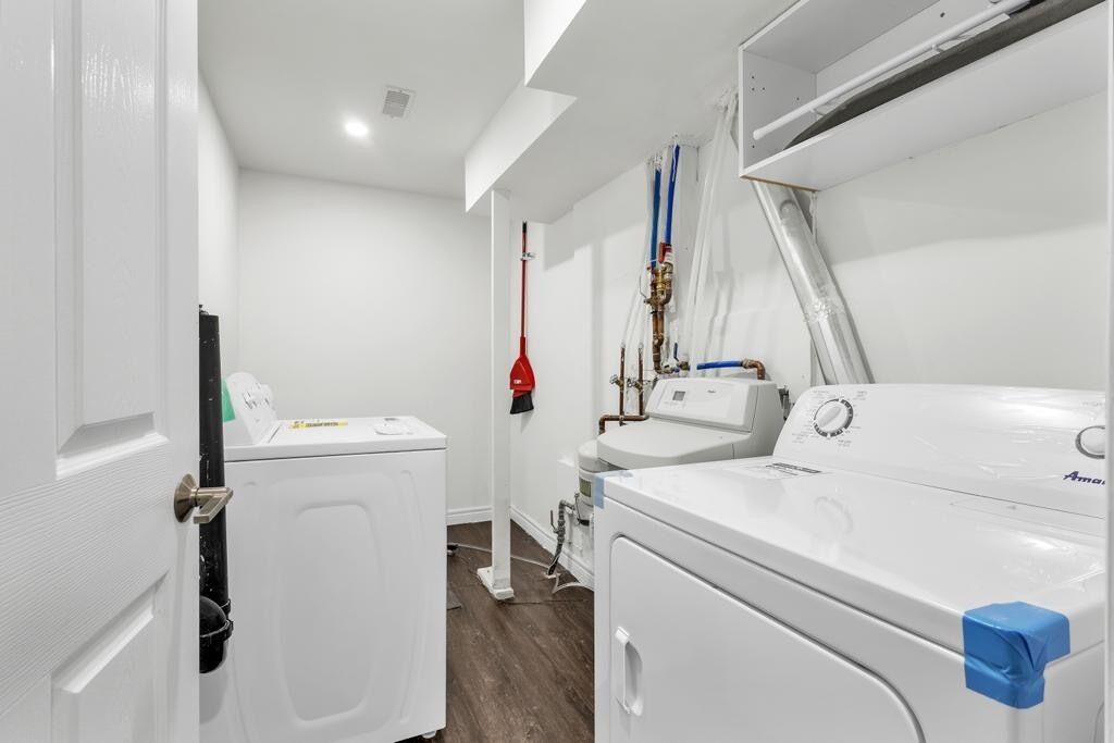 A laundry room with two washing machines, a red mop, and visible plumbing.