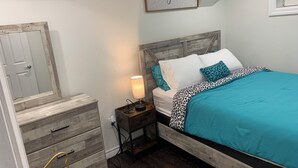 Ein Schlafzimmer mit einem Holz-Kopfteil, einem Bett mit einer blaugrünen Tagesdecke, weißen und leopardenmusterigen Kissen, einer Nachttischlampe und einem an der Wand befestigten Schild mit der Aufschrift 'Zusammen ist unser Lieblingsort'.