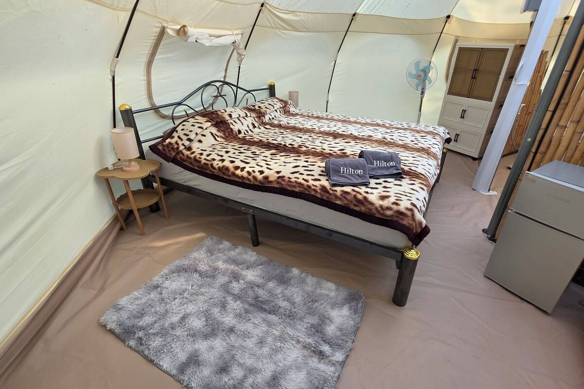 A compact hotel room with a bed, a small bedside table, a fan, and a wardrobe.