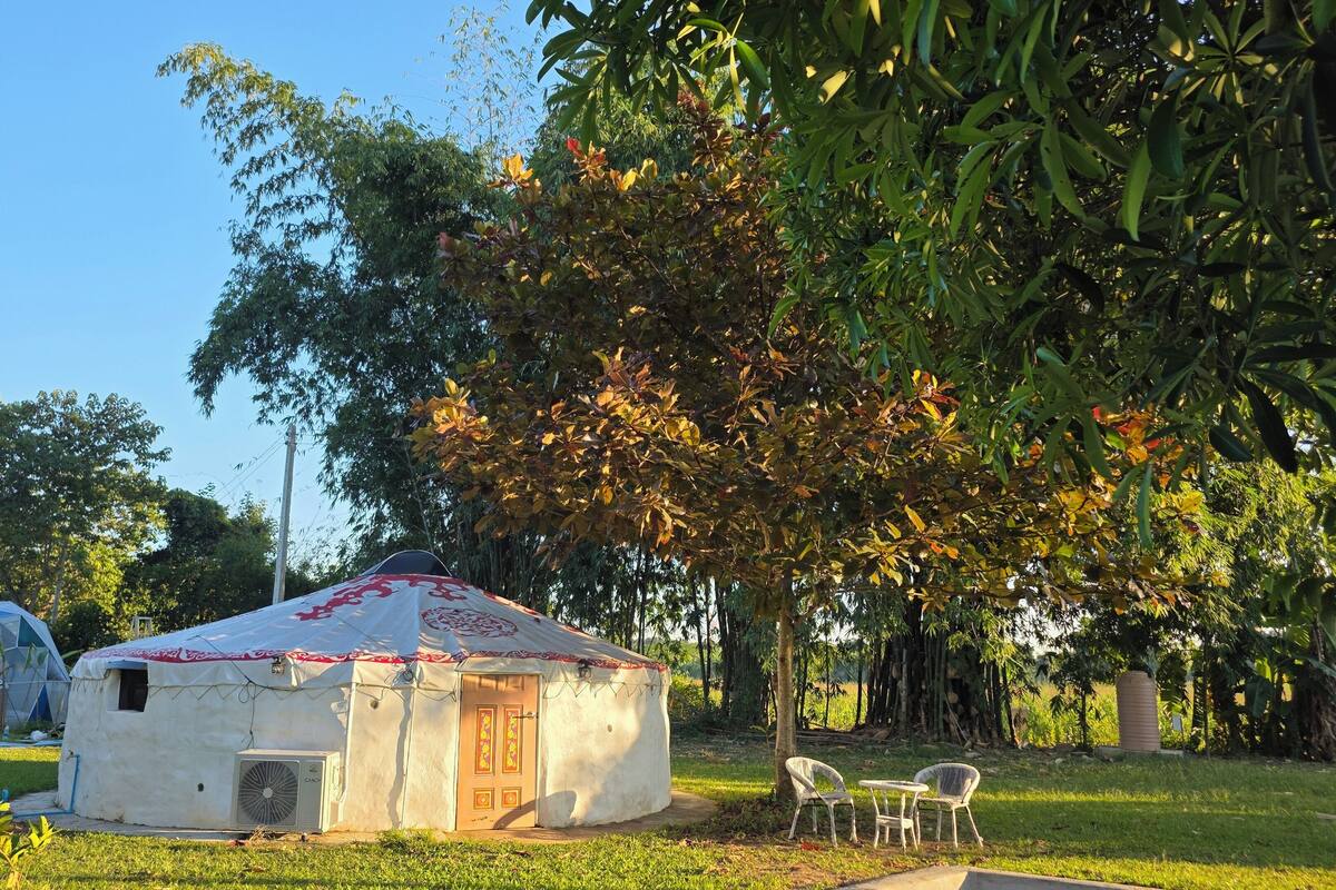 A yurt with a white exterior and red patterns, surrounded by grass and trees.