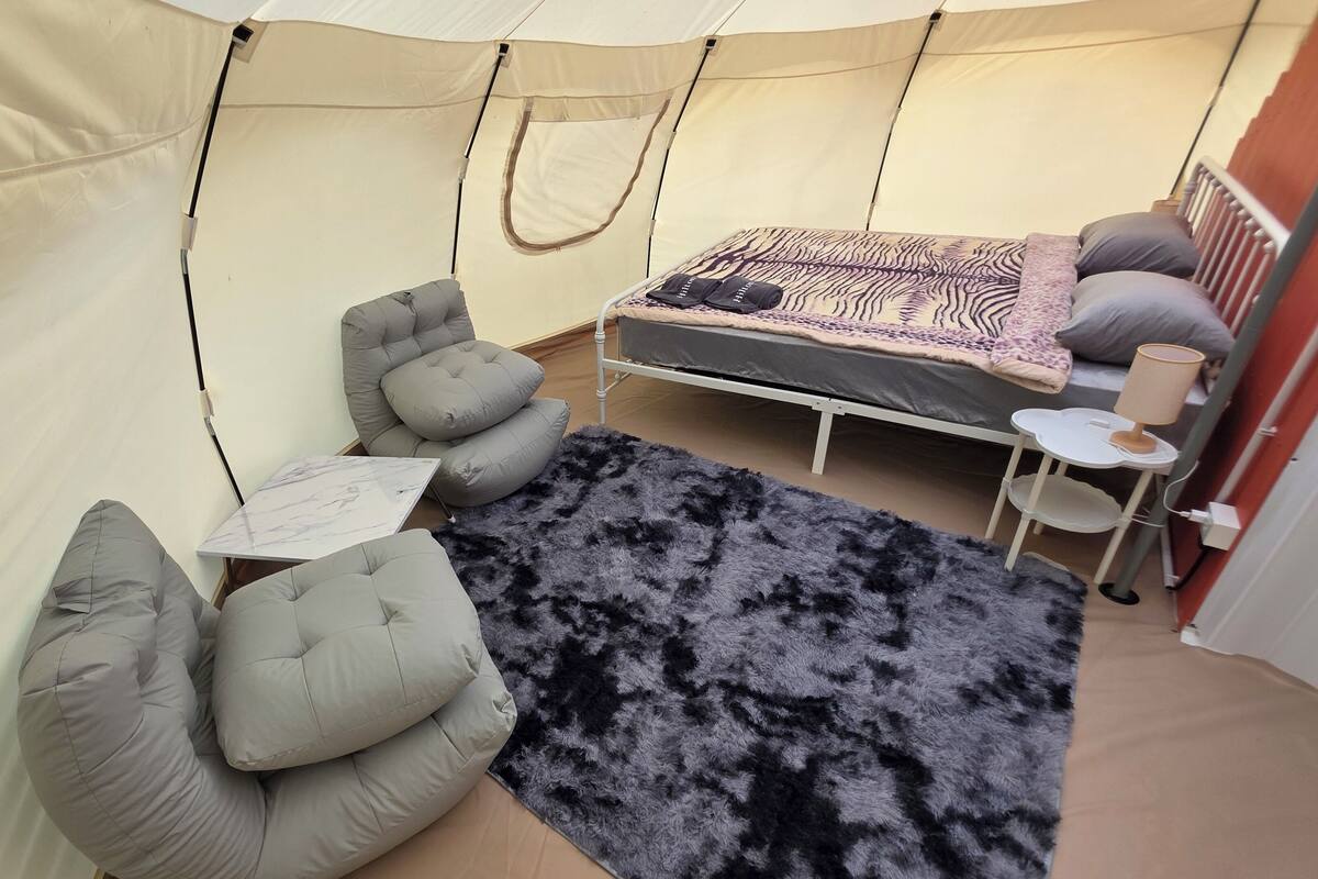 A tented room with a bed, a small table with a lamp, and a sofa.