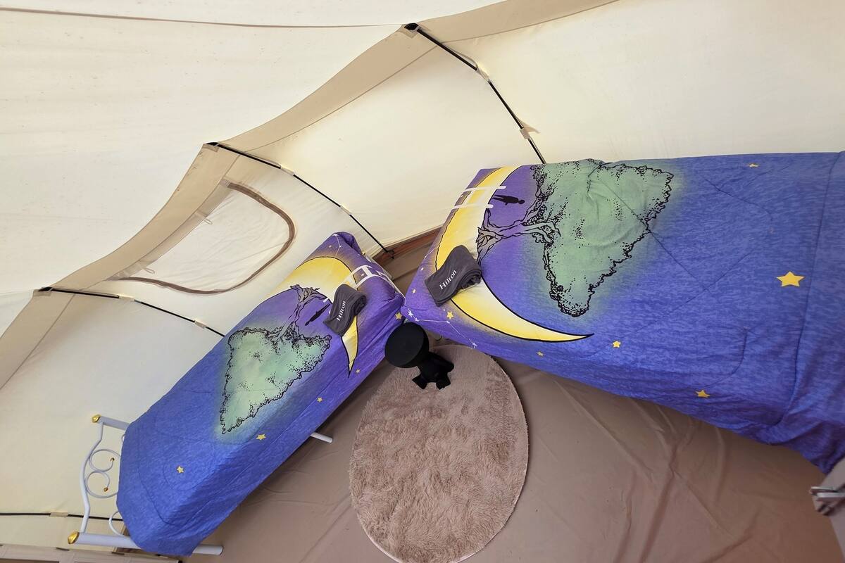 A bed with a blue blanket featuring a moon and stars design, a fluffy round rug, and a white ceiling with a wooden beam structure.