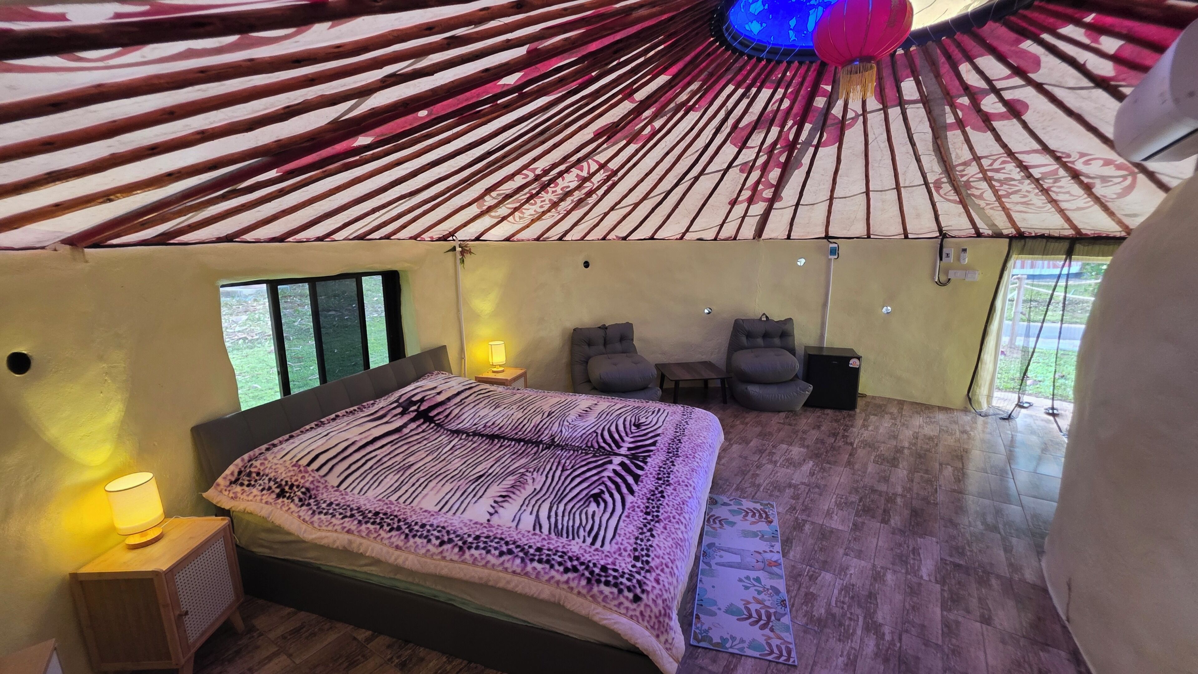 Una habitación con cama, dos sillas, una mesita y un ventanal.