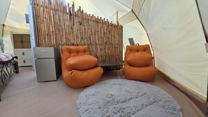 Een kamer met een bamboepartition, twee oranje loungestoelen, een kleine tafel en een koelkast.
