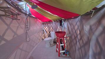 A compact, enclosed space with a shower, toilet, and sink, featuring a red bucket and a ladder.