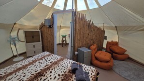 Een tent met een bed, een houten scheidingswand, een wastafel en een stoel.