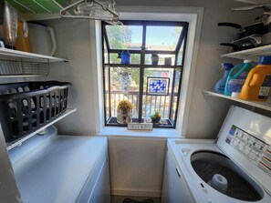 A compact laundry room with a window, a washing machine, a dryer, and shelves with cleaning supplies. - In the trendy, funky & walkable South Congress area — 2-bedroom condo in Austin! (Austin)