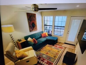 A living room with a green sofa, a patterned rug, a yellow armchair, a lamp, and a ceiling fan. - In the trendy, funky & walkable South Congress area — 2-bedroom condo in Austin! (Austin)