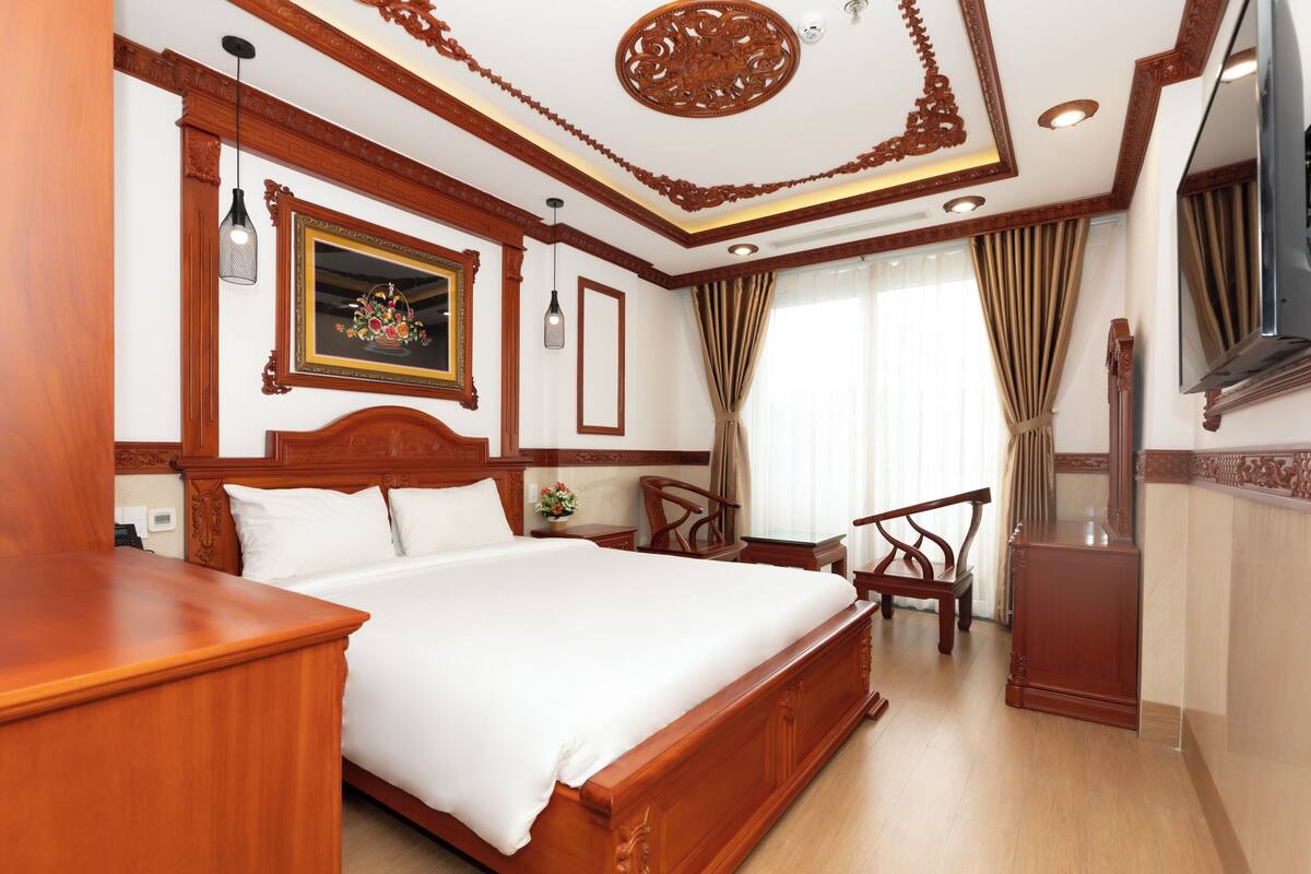 Een hotelkamer met een groot bed, houten meubels, een televisie en een decoratief plafond.