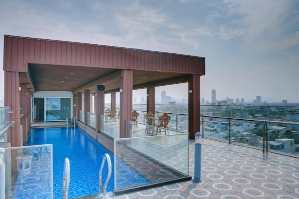 Una piscina sul tetto con barriera in vetro, zona relax e vista sulla città.