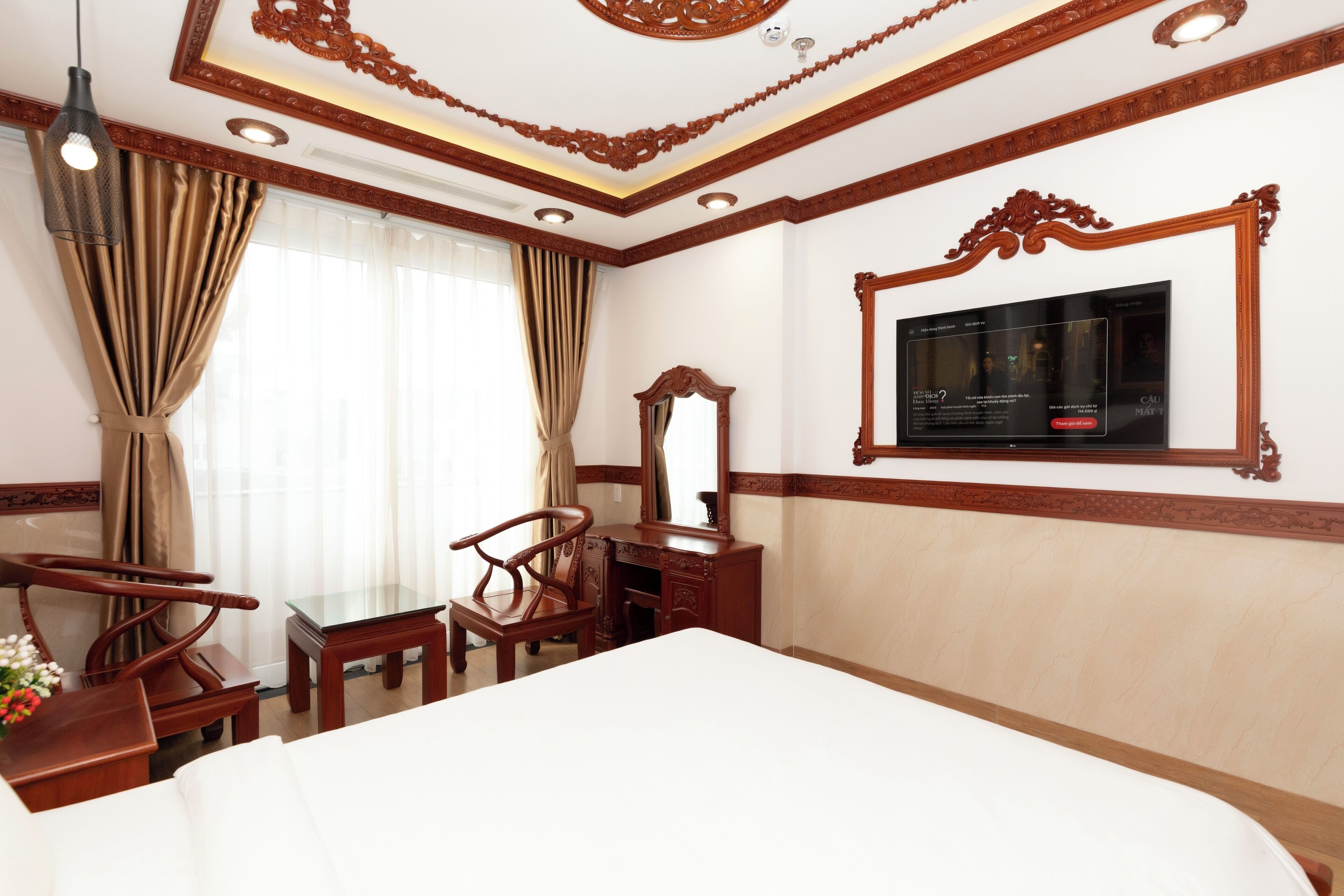 A hotel room with a large bed, wooden furniture, a television, and a decorative ceiling.