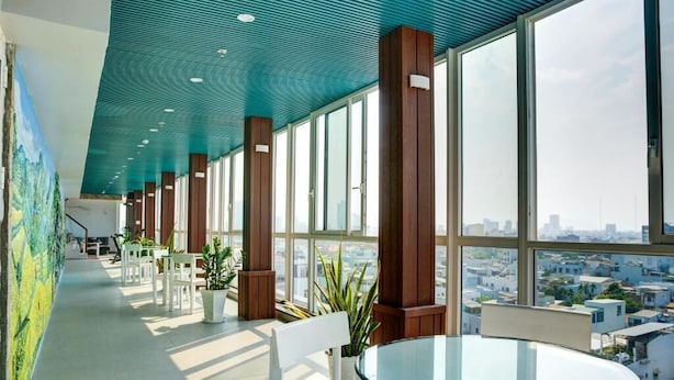 A modern interior with a glass table, white chairs, and large windows offering a city view. - Quan Cuong Hotel (Da Nang)