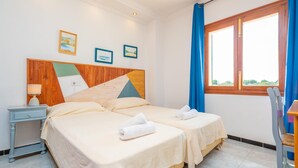 A hotel room with two beds, a wooden headboard, a nightstand, a table, and a window with curtains. - HORABAIXA - Summer house with private pool and WiFi in Portopetro (Santanyí)